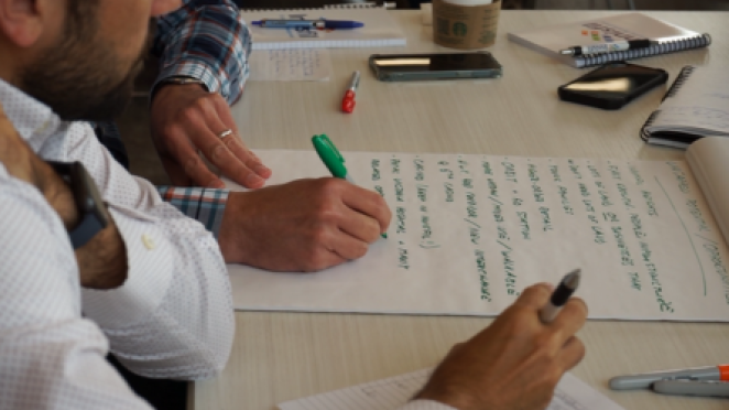 two men sitting and a light desk writing a plan on a large piece of paper surrounded by coffee and mobile phones