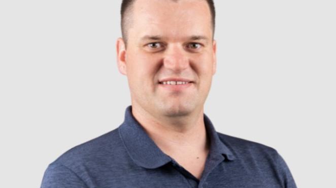 Jelmer Stegink, a man wearing a blue polo short with brown hair smiling in front of a grey background
