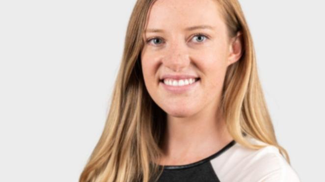 Kate Quigley, a woman with long blond hair wearing a baseball T smiling in front of a grey background