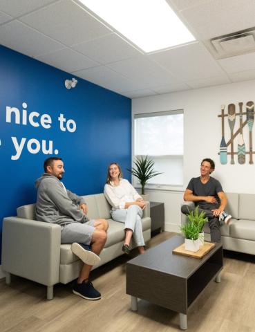 Group of 3 people sitting on grey couches chatting in an office setting
